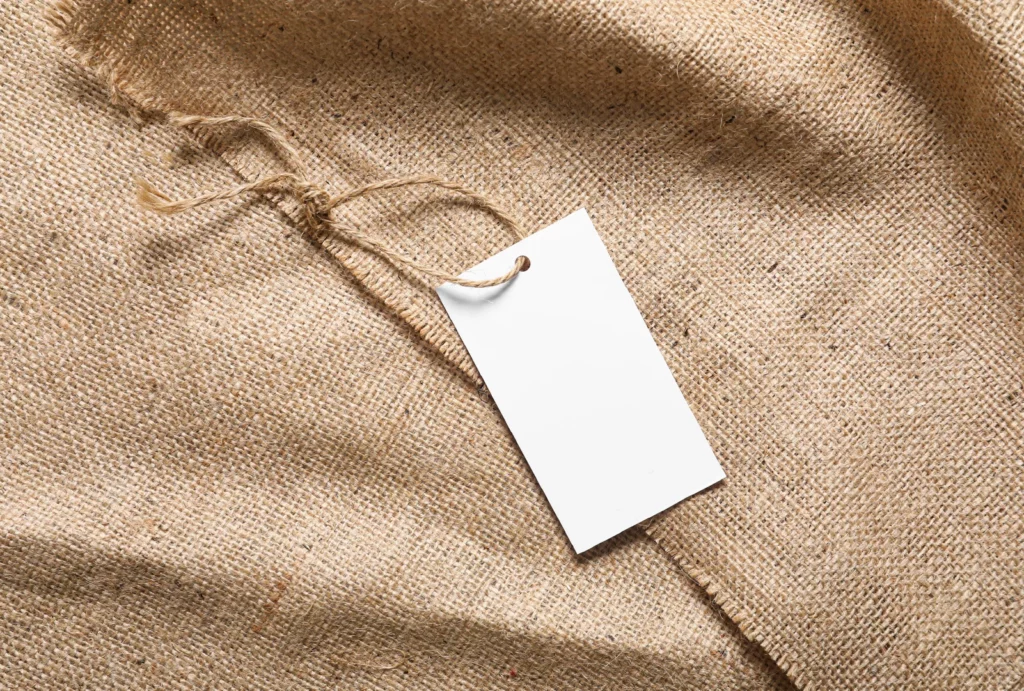 A white product label looped with twine and set atop rolling burlap fabric.