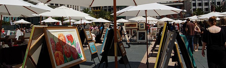 A row of umbrellas and tents at an outdoor art show to help keep customers and vendors cool from the heat.