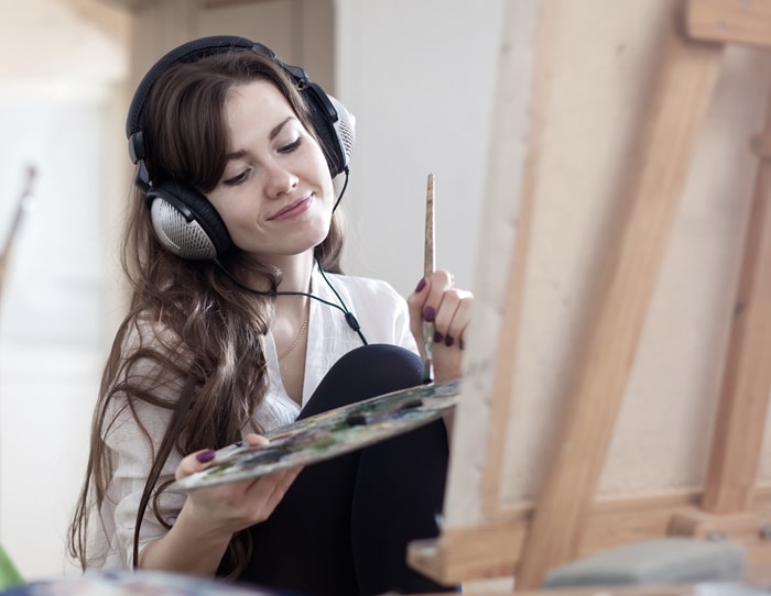 A girl paints with headphones on.