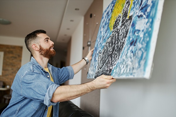 A man hangs a custom painting on his wall in his living room.