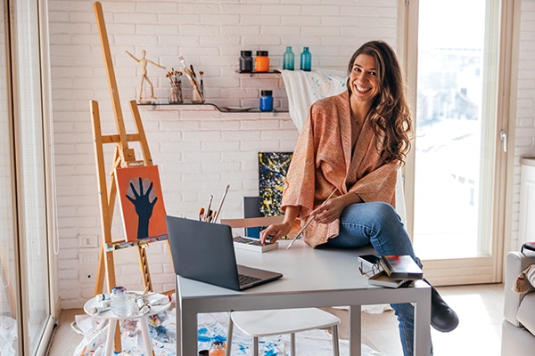 A young woman painter works with different art mediums to complete a project in her home studio.