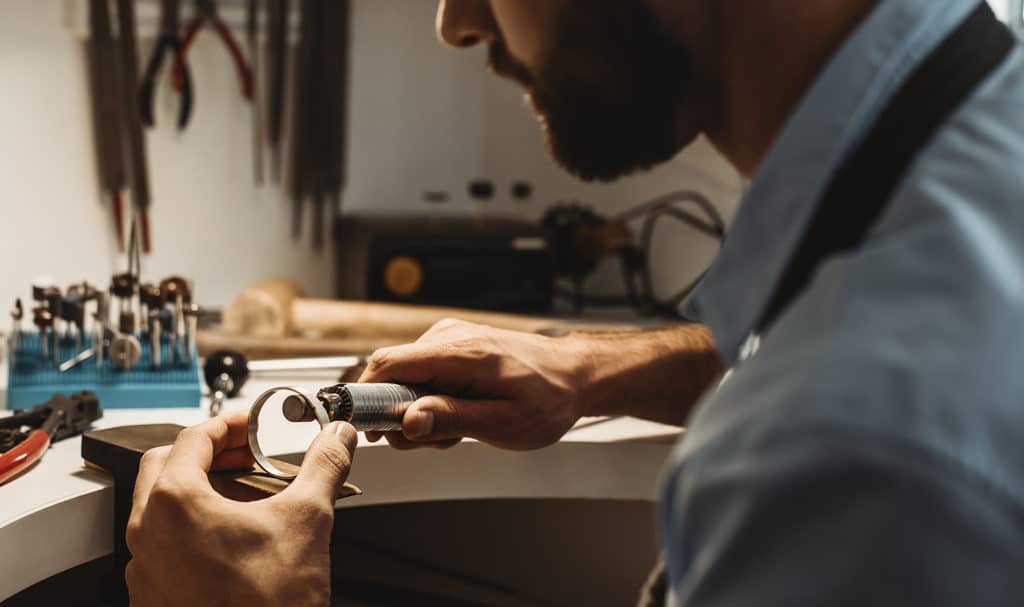 A man uses a jewelers tool to smooth down the inner edges of a gold hoop he is working on in his studio.