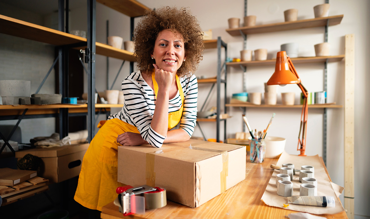 A woman leans on a box on a table in her home art studio.