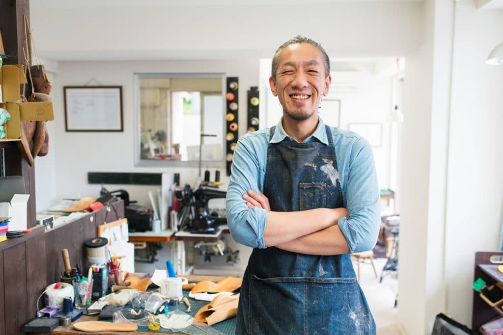 An artist smiles in an art studio with their arms crossed.