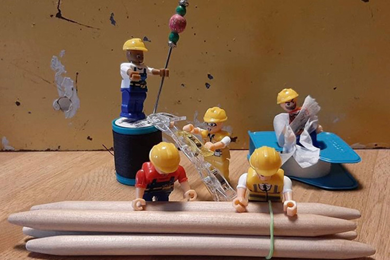 Mini construction worker figurines are displayed in a way that looks as if they are using Joan's sewing tools as construction tools.