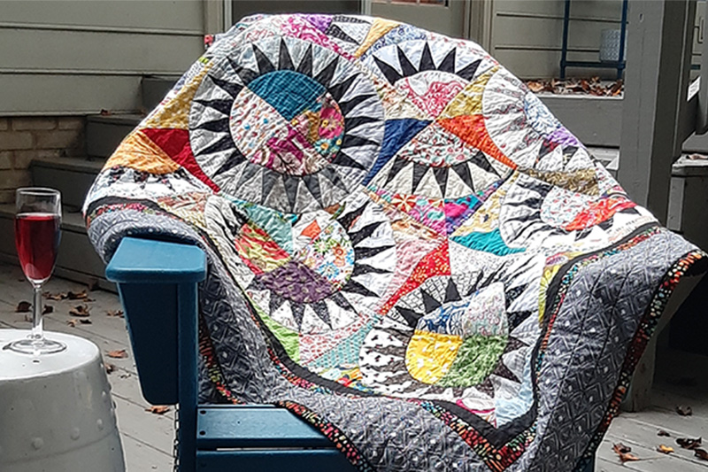 One of Joan's colorful and patterned quilts is laid out across a chair in her backyard.