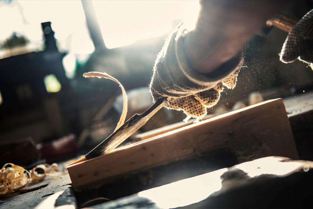A chisel shreds off a layer of wood from a block.