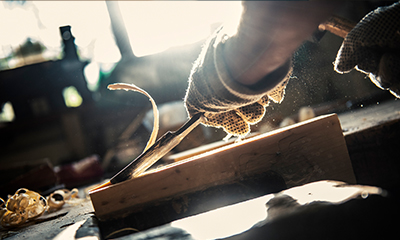 A chisel shreds off a layer of wood from a block.