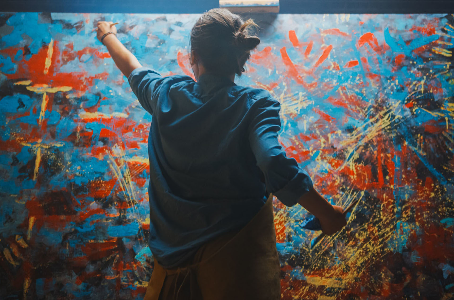 A woman in blue paints on a large canvas or panel.