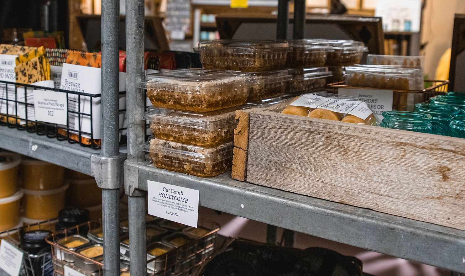 Handmade beeswax candles, soaps, food wrap, and more are perfectly displayed in boxes and crates on metal shelves in the Farm and Hive booth.