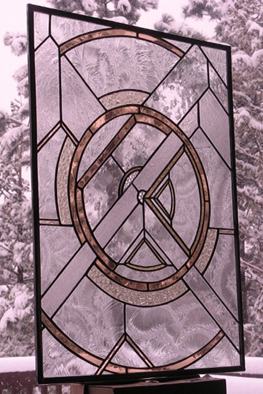 A stained glass window using mostly opaque and white colors is assembled in a geometric pattern of circles and triangles. The snowy view outside is showing through parts of the glass.