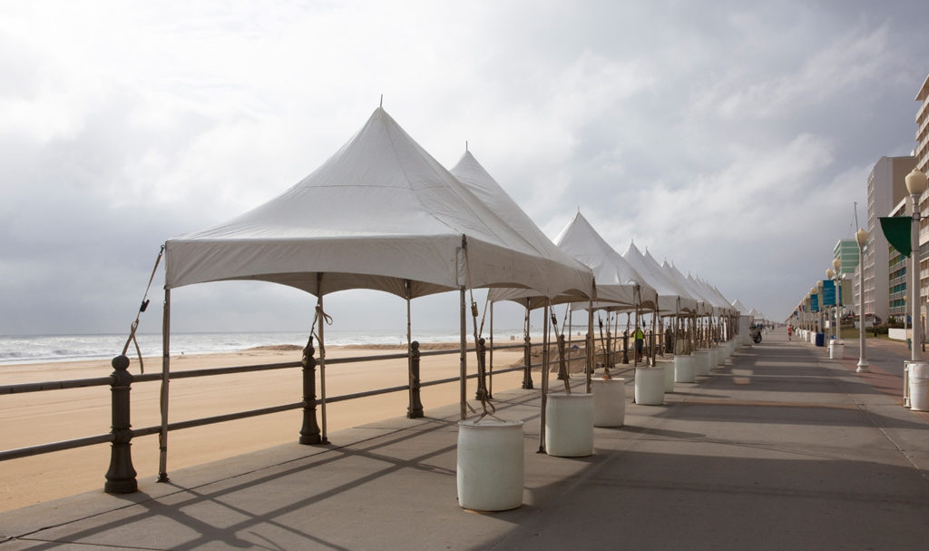 A row of empty white vendor booth tents are lined up along a boardwalk as an impending storm brews in the distance.