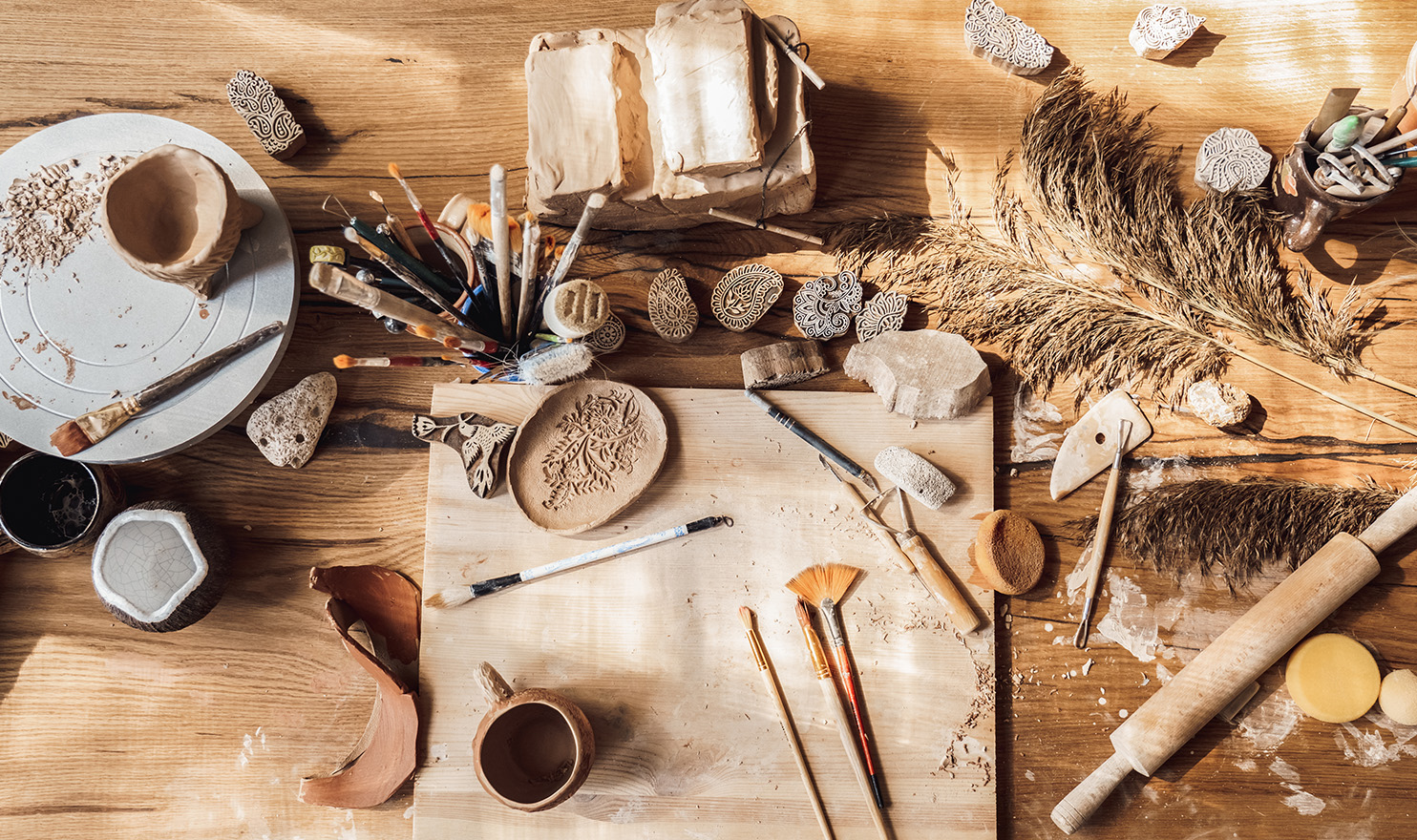 A set of clay and pottery tools lay on a crafting table in the home studio of an artist.