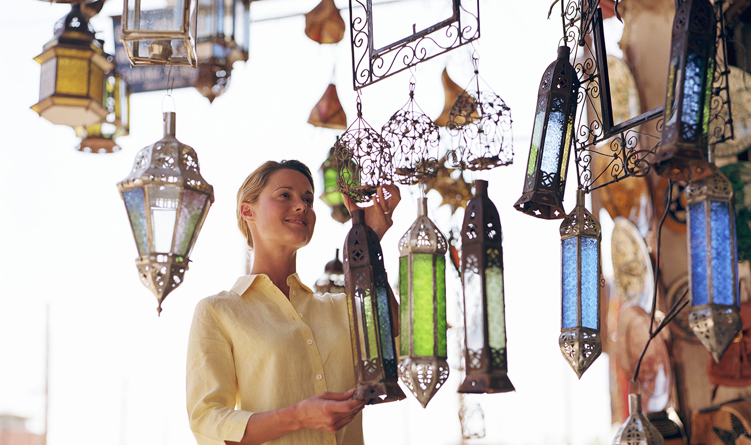 A woman is looking at the handcrafted glass on the lights hanging in a vendor tent at an outdoor event.