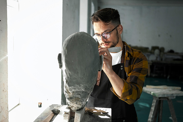 A sculpture works on a bust.