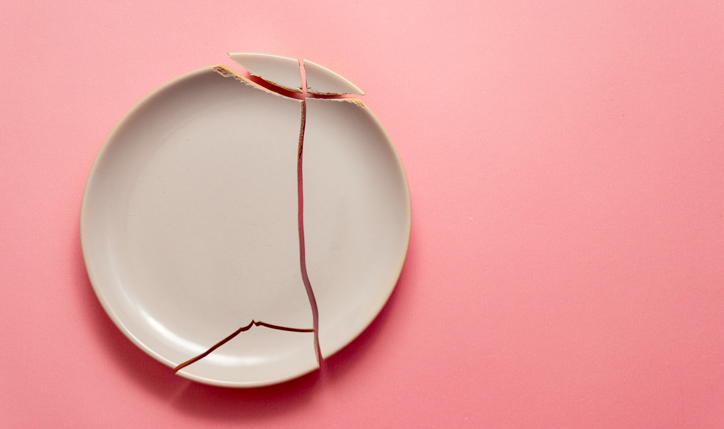 A broken clay plate on a light pink background.