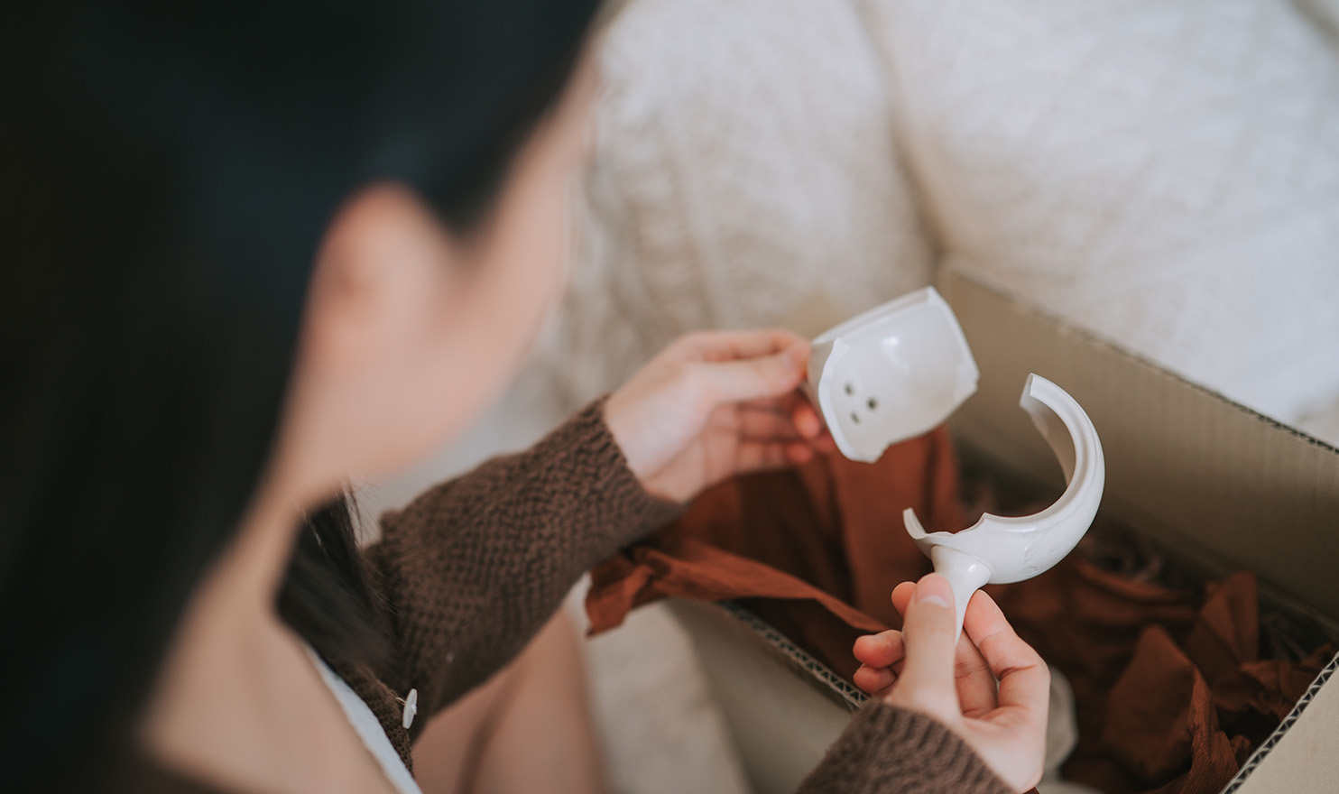 A person holding a broken handmade teacup that was damaged during shipping and poses the risk of hurting the customer.