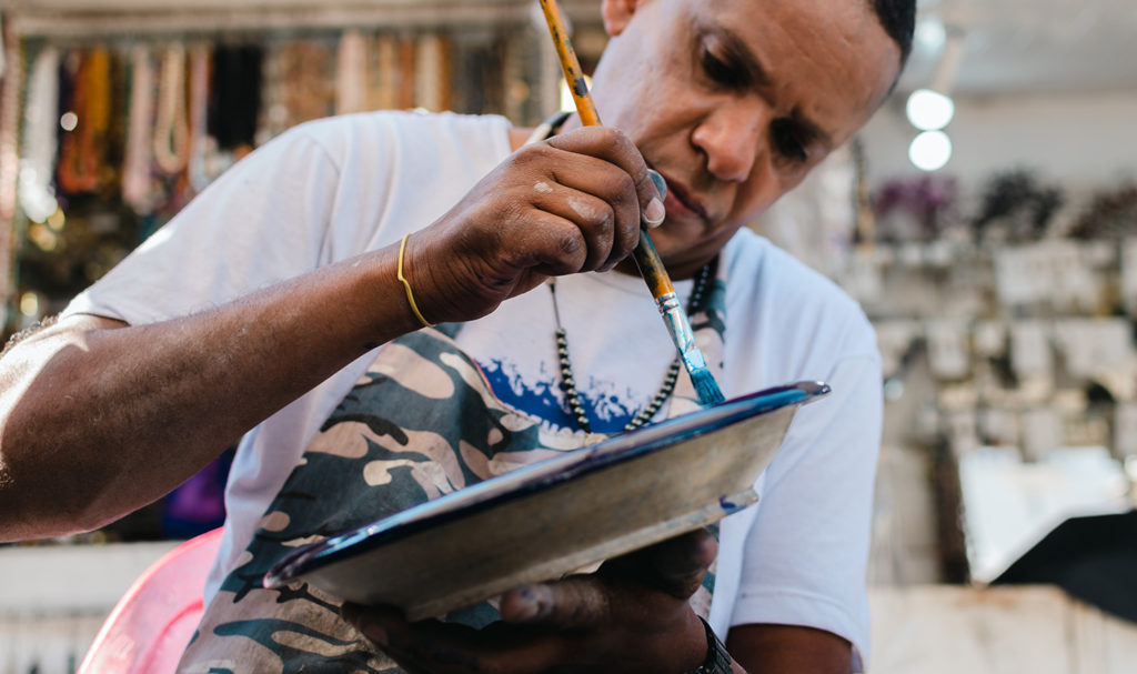 A vendor is working on painting another plate during some down time in his booth at an event.