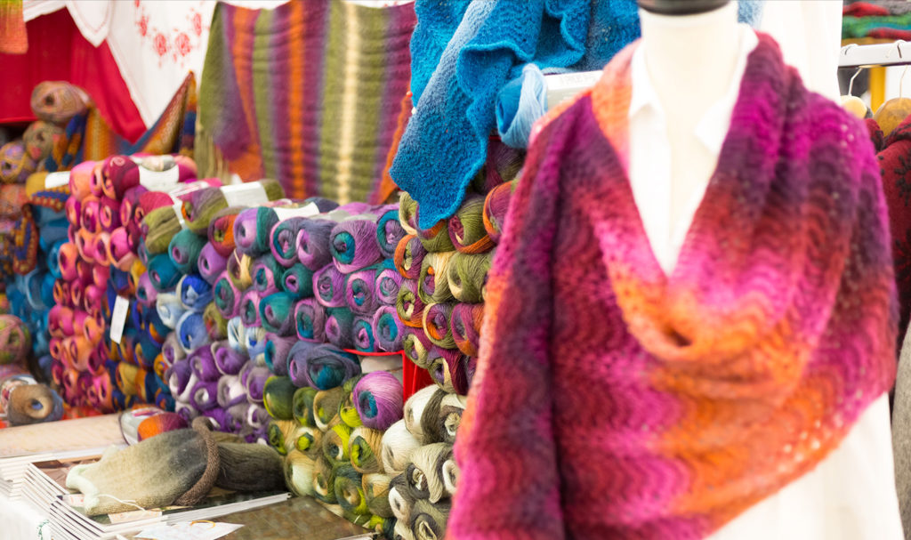 A handknitted scarf is on a mannequin next to other handmade products in a vendor's craft show booth.