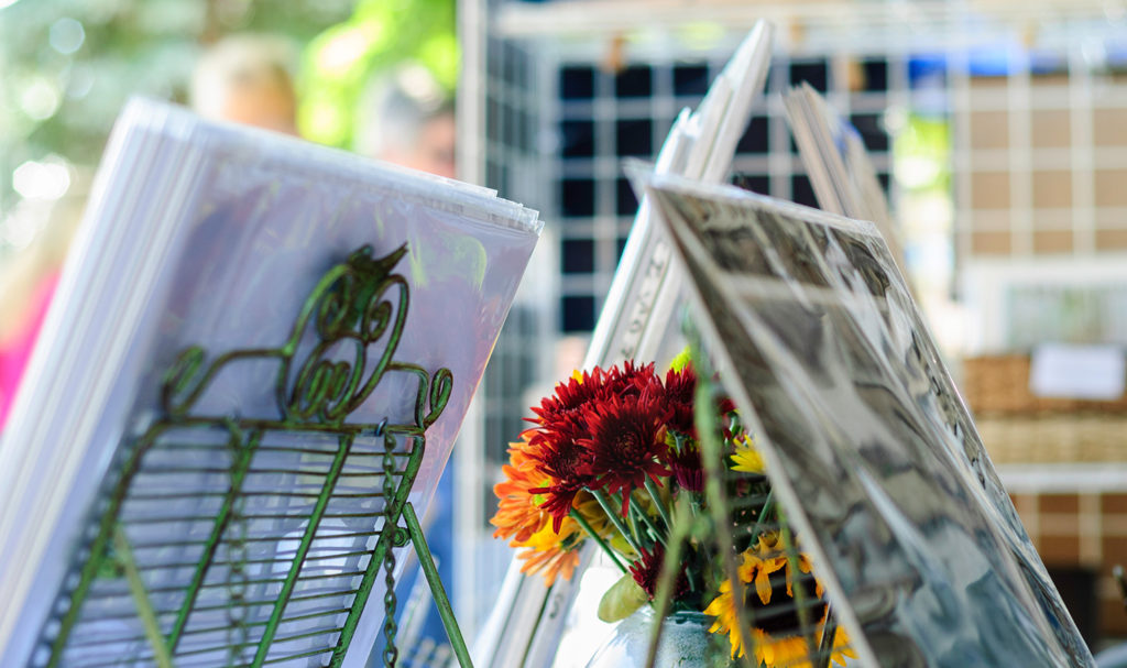 A set of painting are on display on easels in a vendor's booth at a craft show.