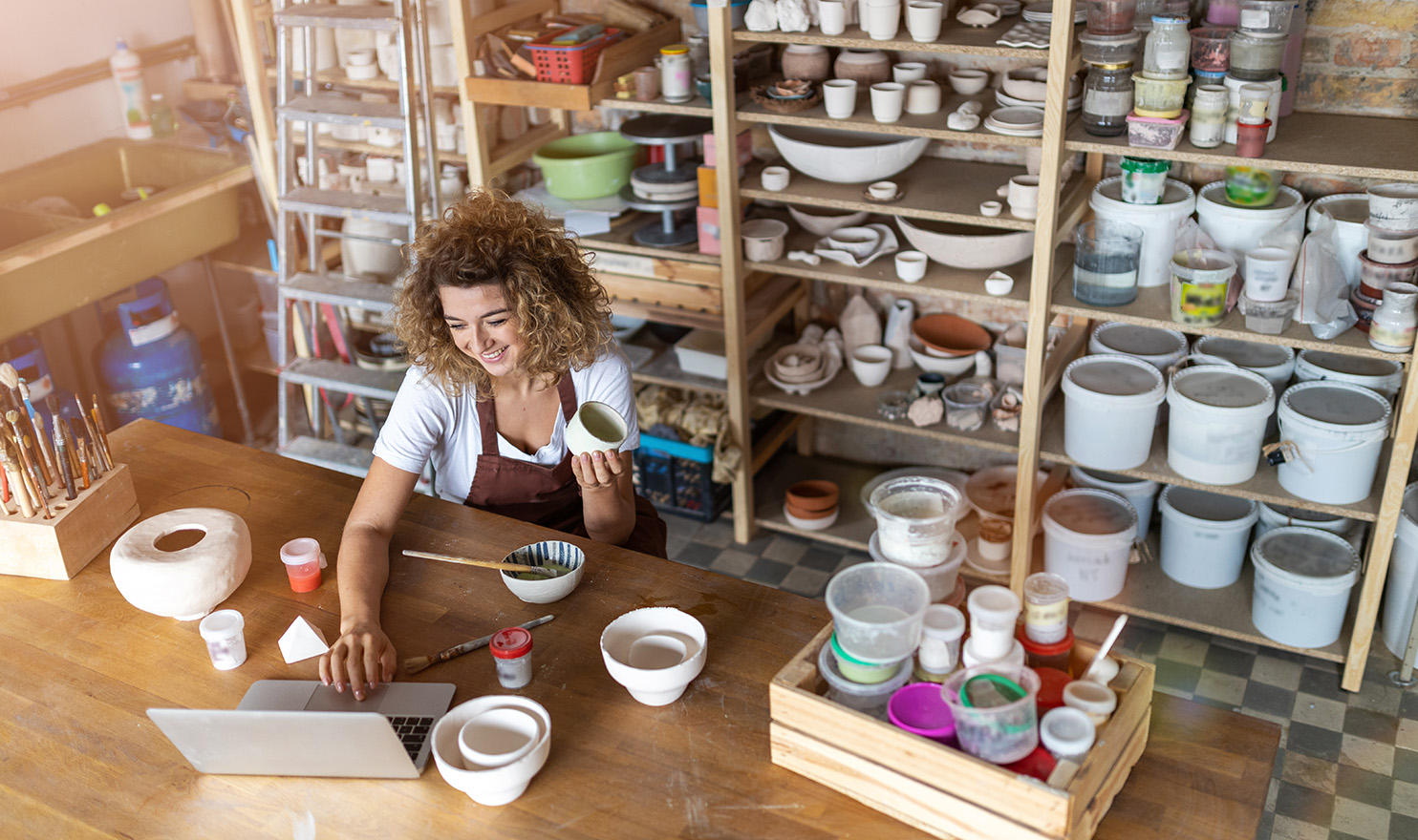 A pottery business owner is updating her website in her pottery studio.