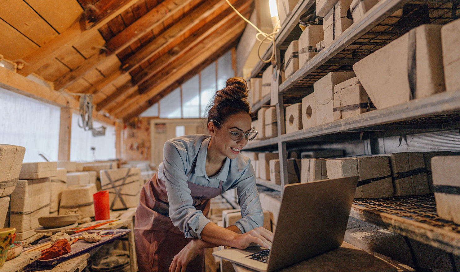 A crafter is in her workshop smiling at her laptop propped up on her workstation as she writes a blog based on her latest piece she created.