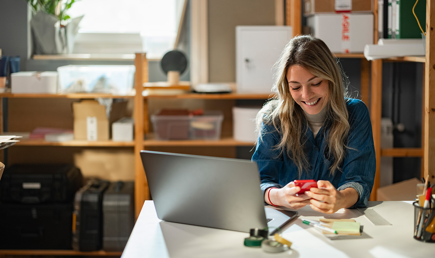 A young businessowner is in her studio on her laptop and phone as she works on her marketing plans.