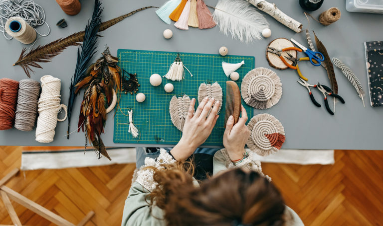 An overhead shot of a woman working on crafts in her workshop on items she will sell in her online Etsy.