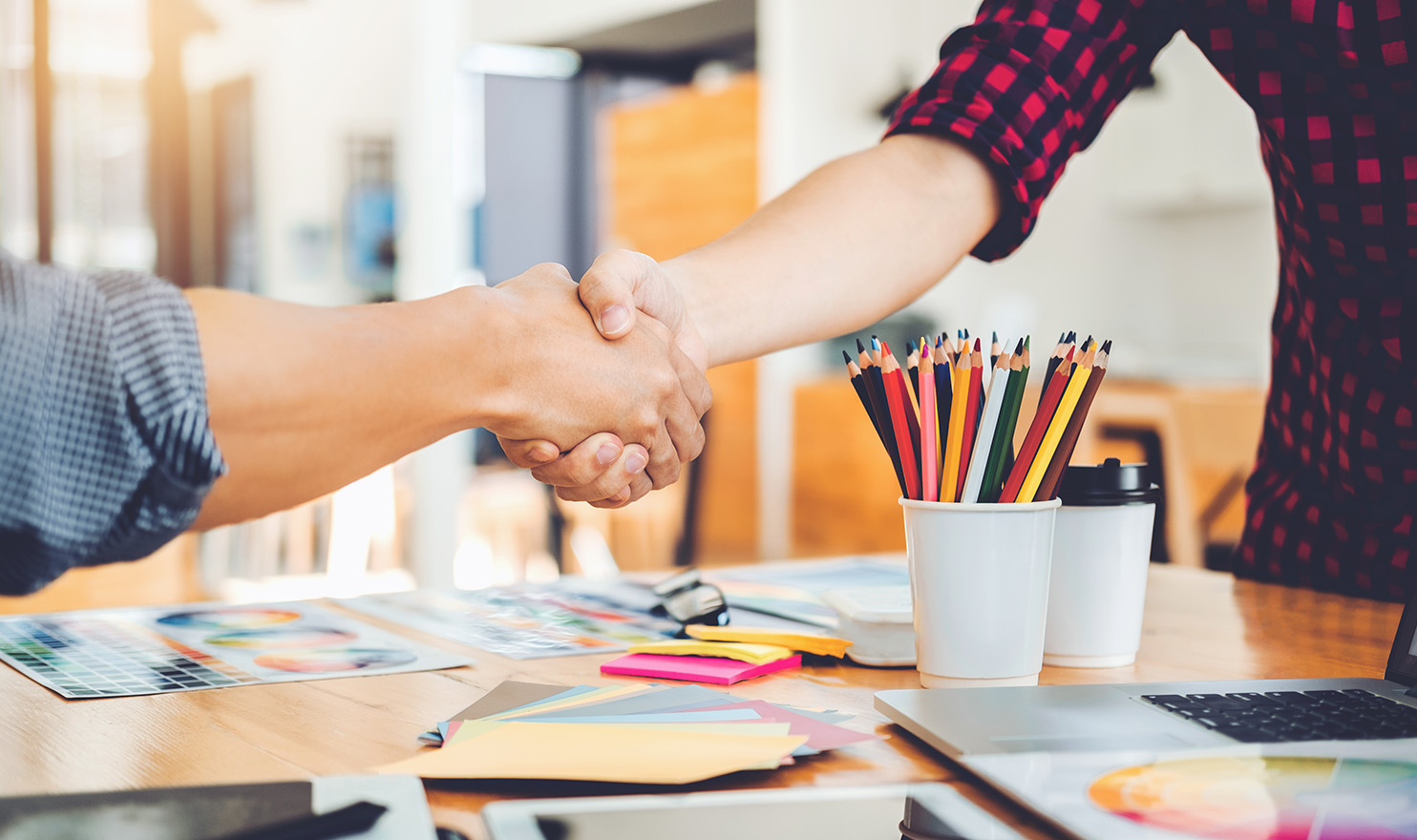 A business owner and a customer shake hands over a desk with art supplies.
