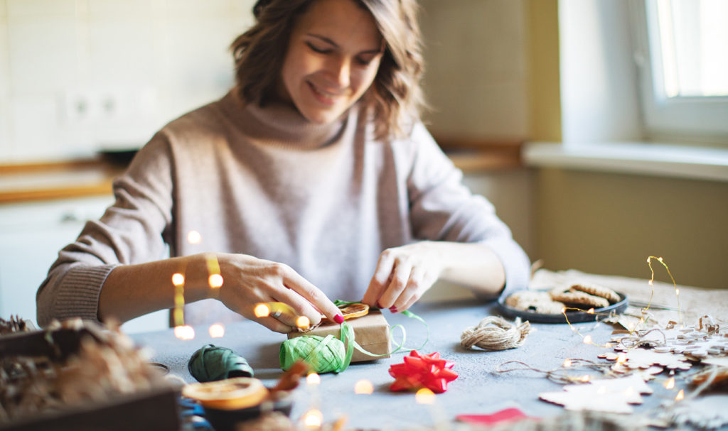 A handmade business owner is preparing one of their product in their holiday packaging for a customer.