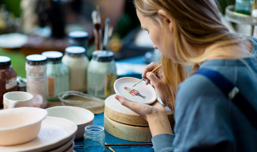 An artist works on painting handcrafted dishes for her creative online business.