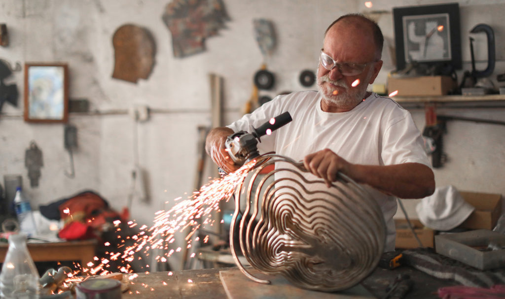 A metalworker is sanding down a product he made in his workshop.