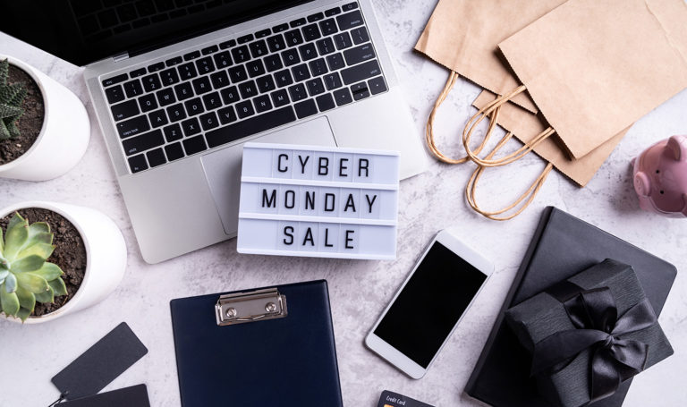 An overhead shot of a laptop on a workspace filled with bags, a notebook, a phone, glasses, office supplies, and a letterboard sign that says "Small Business Saturday"