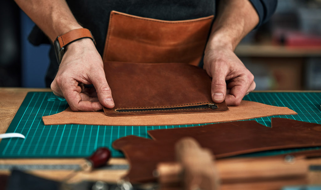 A leatherworker crafting with a hide at their workstation surrounded by their tools.