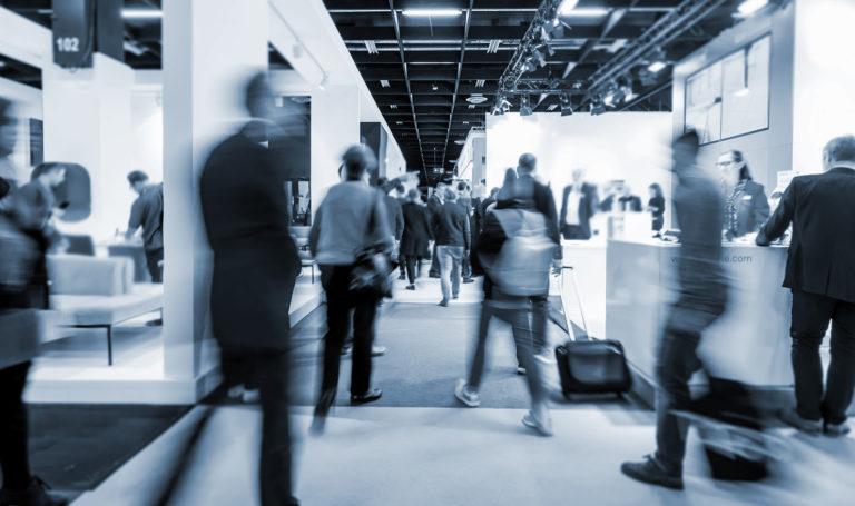 A black and white visual of a trade show with customers moving around to visit each booth. Our trade show booth ideas can help you booth stand out at a busy event and attract customers.