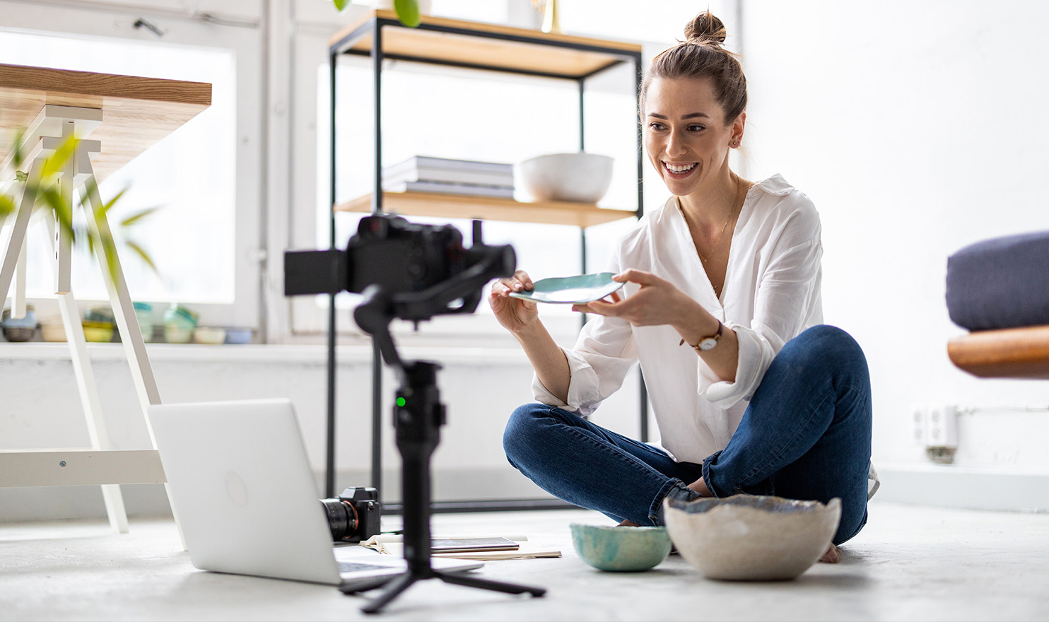A crafter is siting on the floor of her studio in front of a phone on a tripod as she goes live on social media to show off her latest creations.