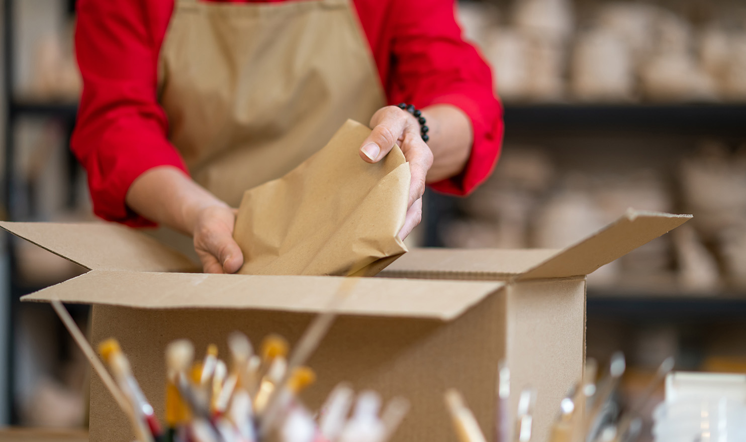 A crafter is carefully wrapping and packing up a handmade item for shipping.