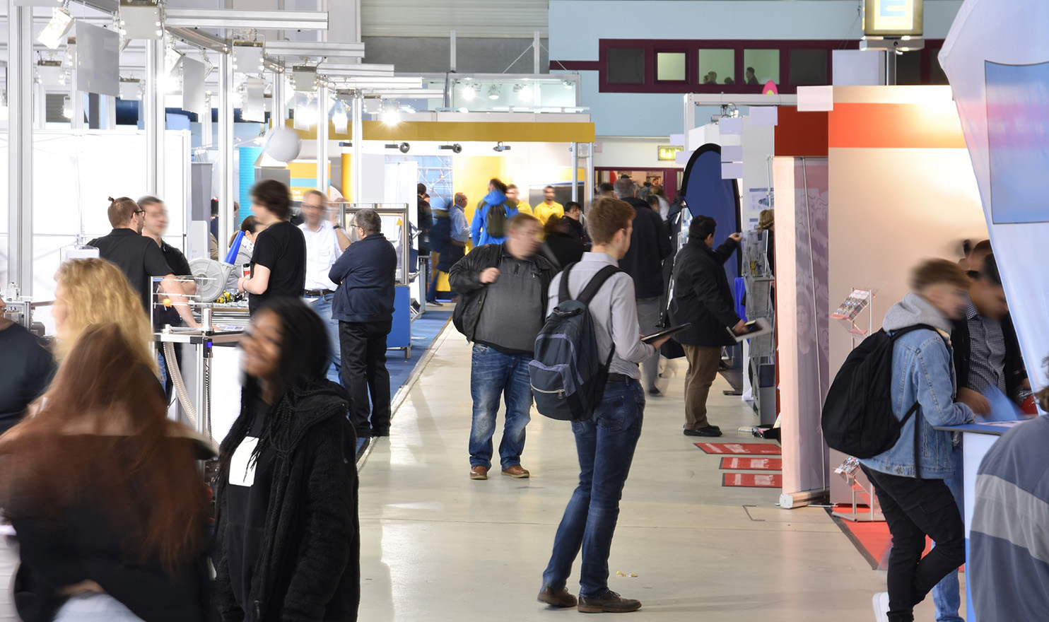 A view of an event hall lined with trade show booths and patrons shopping among them.