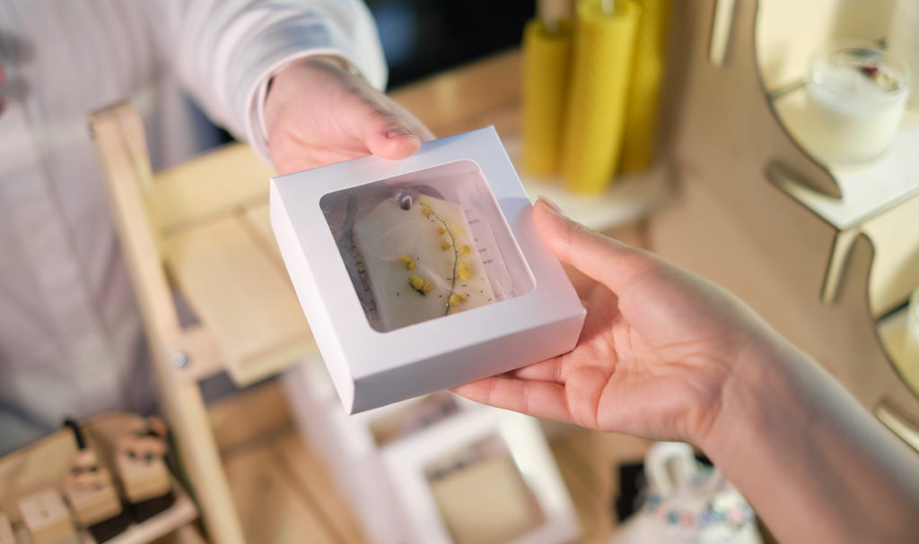 A close up shot of a vendor's hands passing a boxed product to a customer.