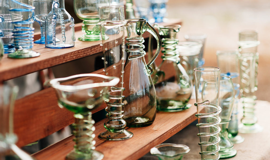 A row of handmade glass bottles sit on a wooden display at a festival.