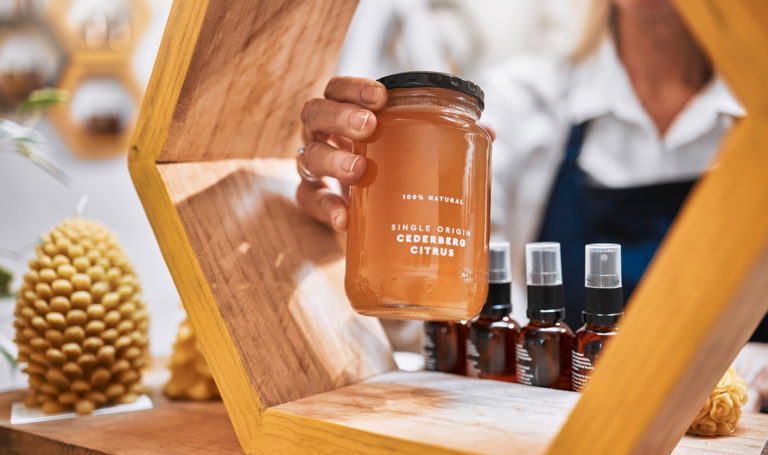 A close-up view of a vendors hand placing a jar of honey out on a display on their booth table. It can be helpful to see other vendors' set-ups at a show so you can get vendor booth display ideas.