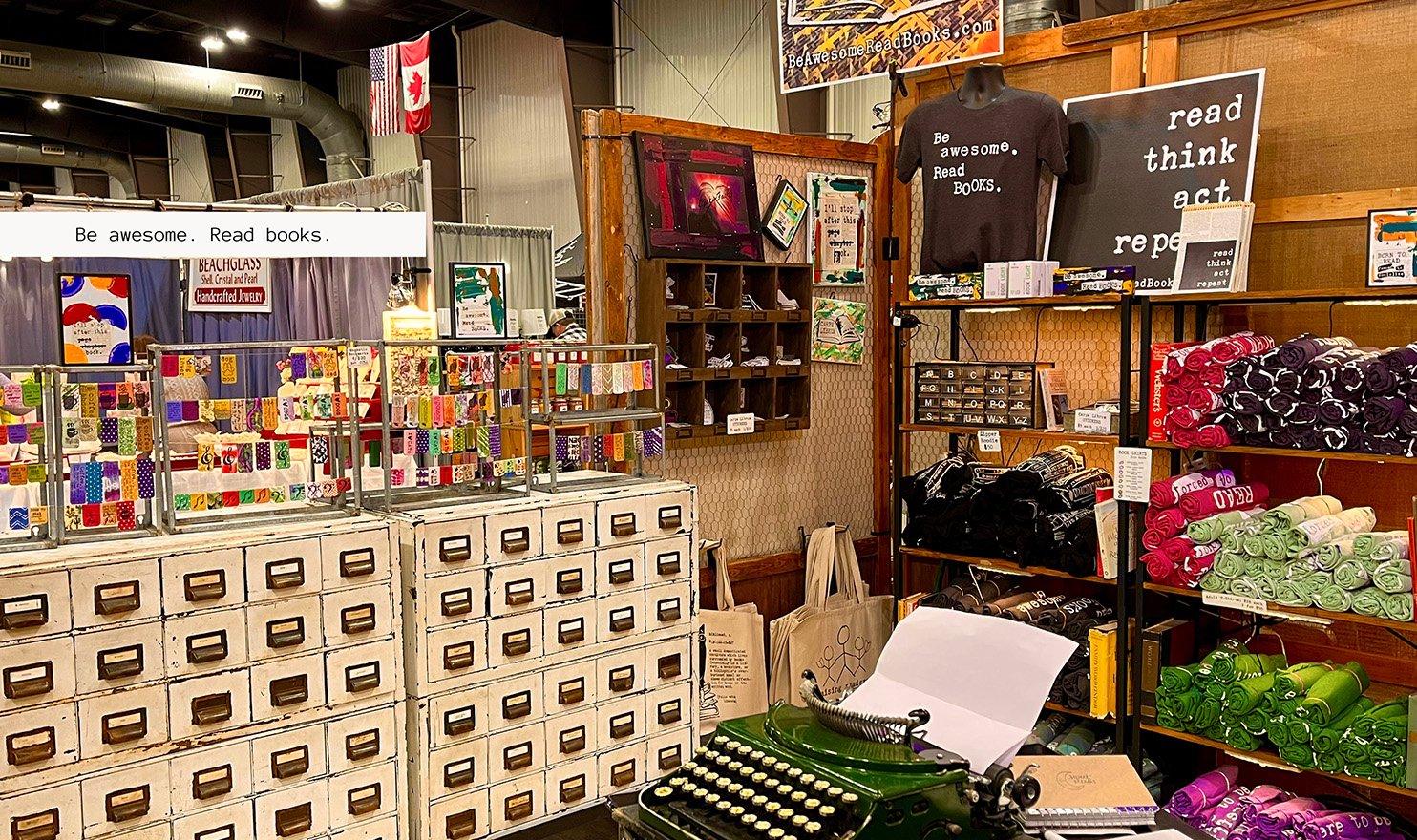 Elizabeth's booth display at an event. She uses a lot of vintage filing cabinets, old typewriters, and vintage shelving to display her tshirts, tote bags, and bookmarks.