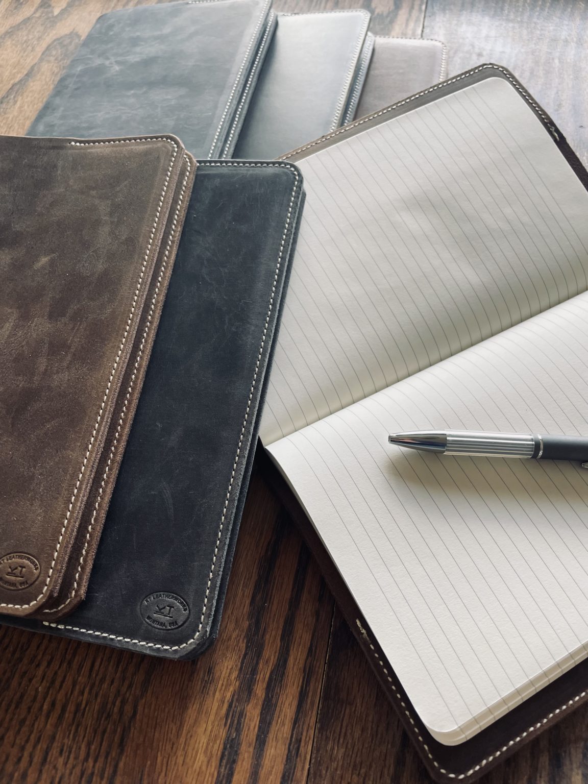 Three leather journals Kelsey handcrafted are laying out on a table, with one of them opened to show the paper inside.