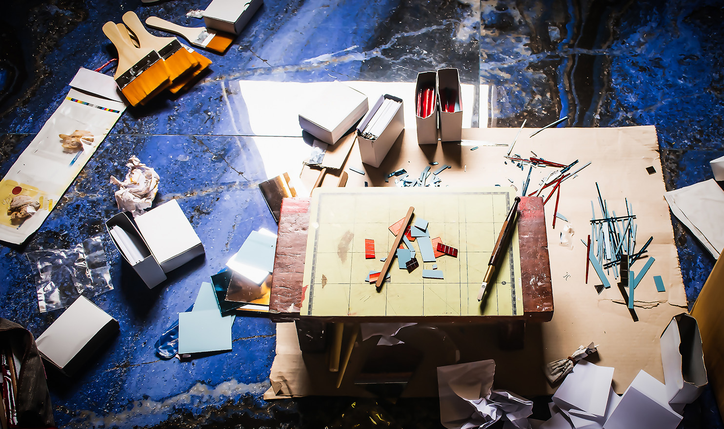 An overhead shot of a variety of crafting tools lay scattered on a small table and a blue tarp on the ground.