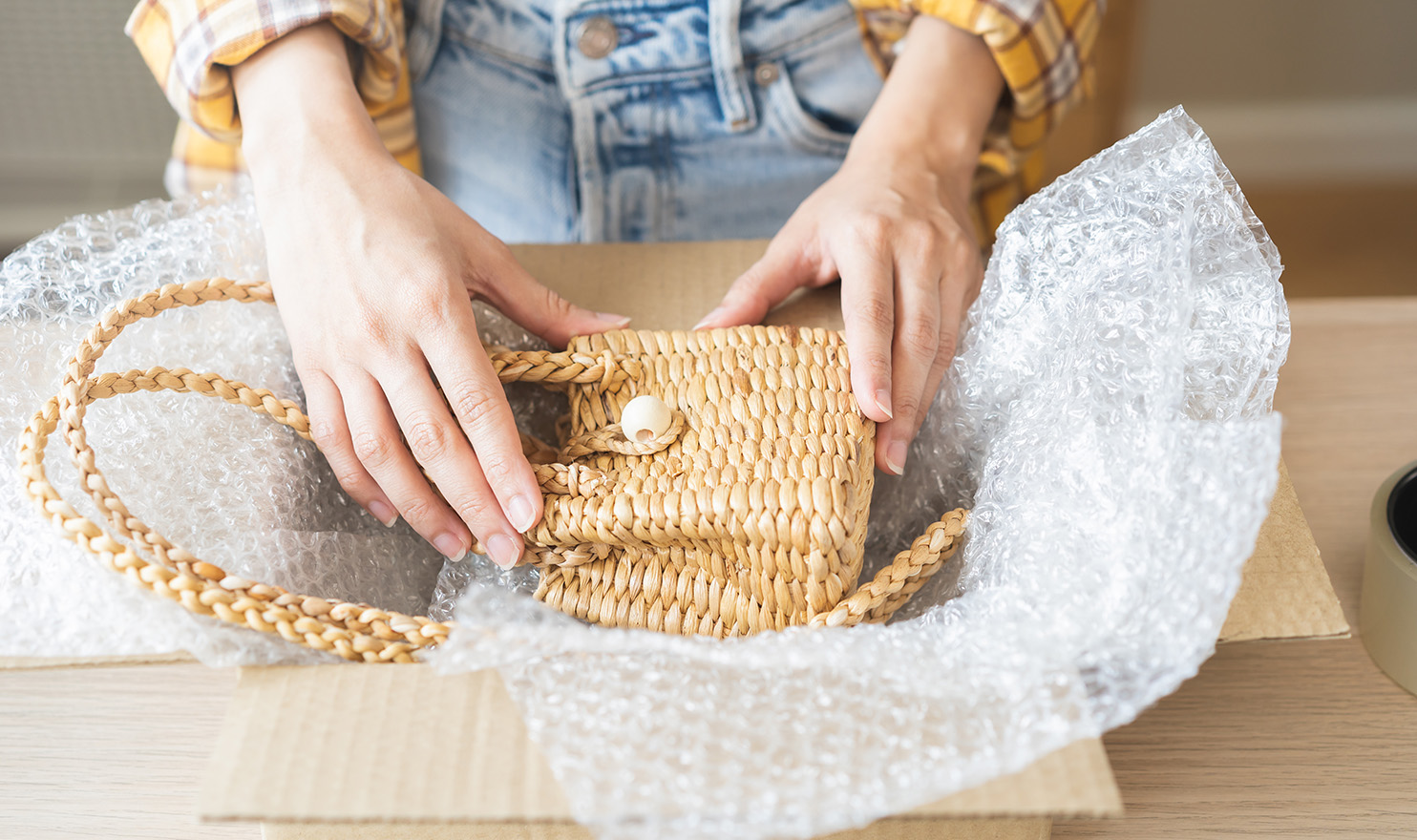 An artist's hand are carefully placing a handmade purse into a shipping box.