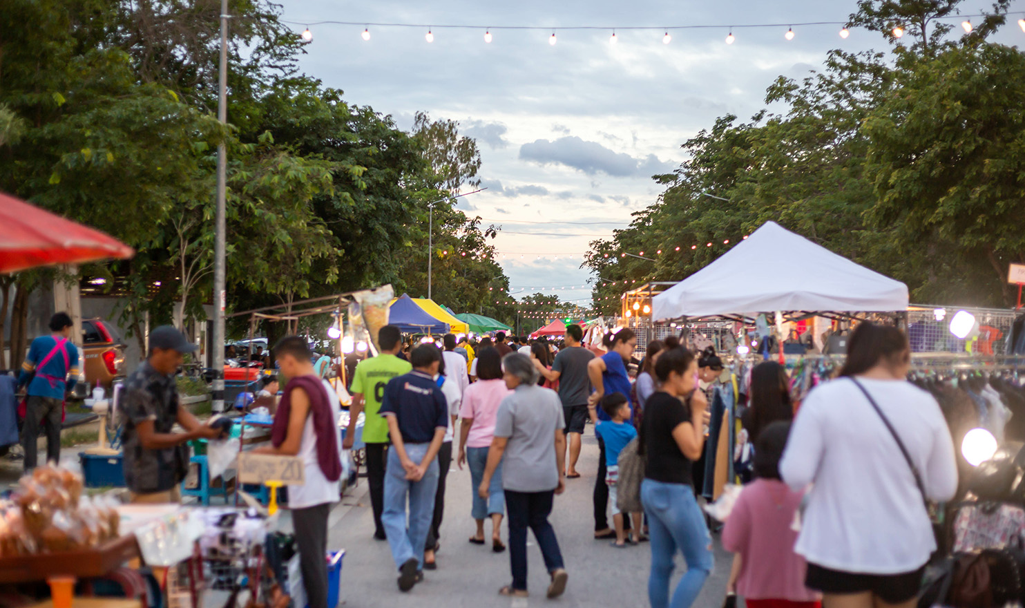 A row of vendor booths line a busy outdoor craft show full of local shoppers.