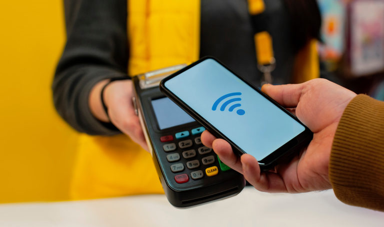 A person is using a mobile smartphone to scan a payment system and complete a transaction. There is a solid yellow background behind the vendor holding the payment system.