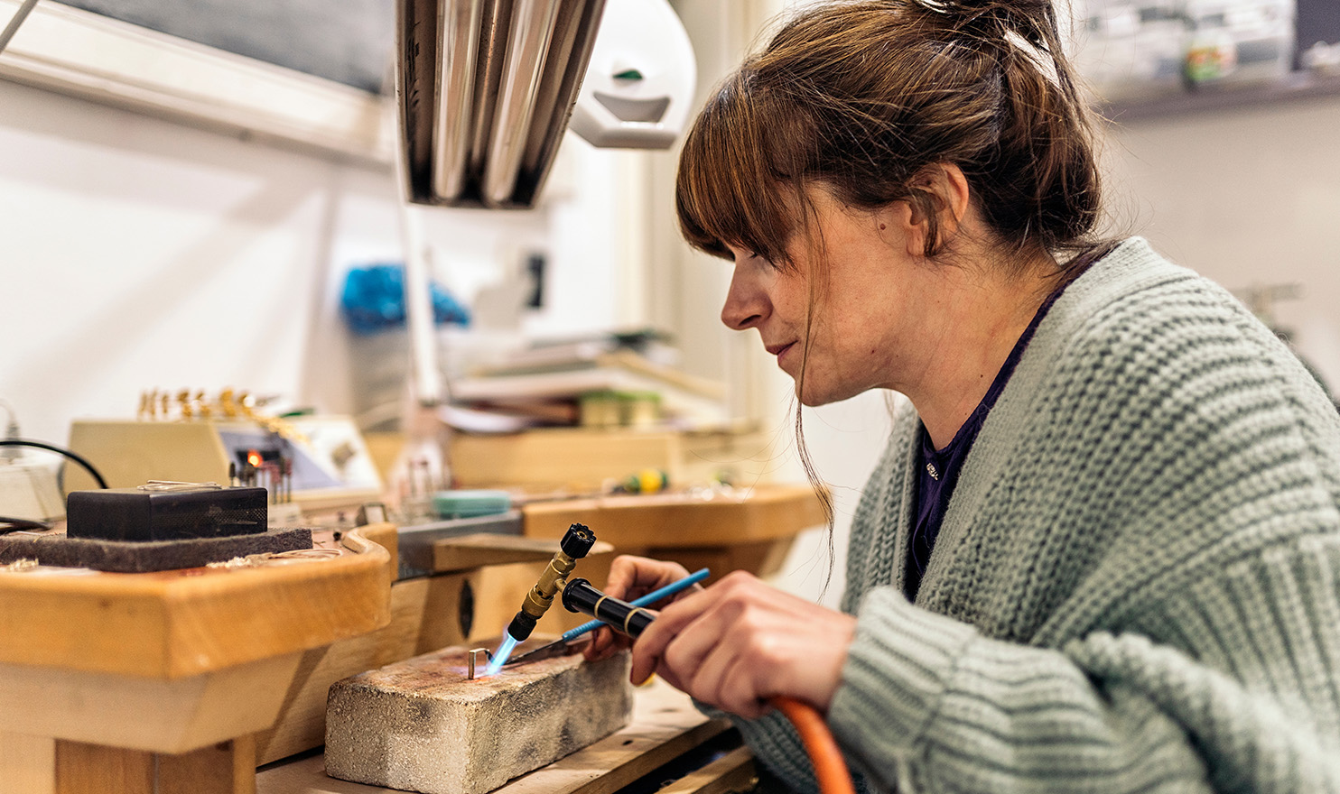 A jeweler is crafting a new piece in their workshop with various tools.