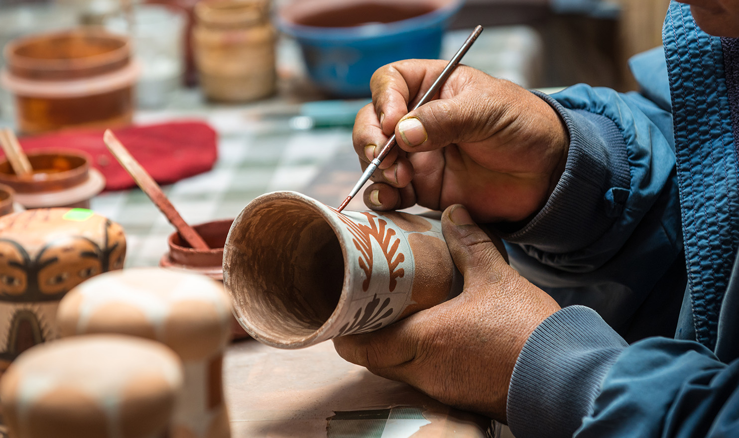 An artisan is very carefully painting a design onto a handcrafted piece of pottery.