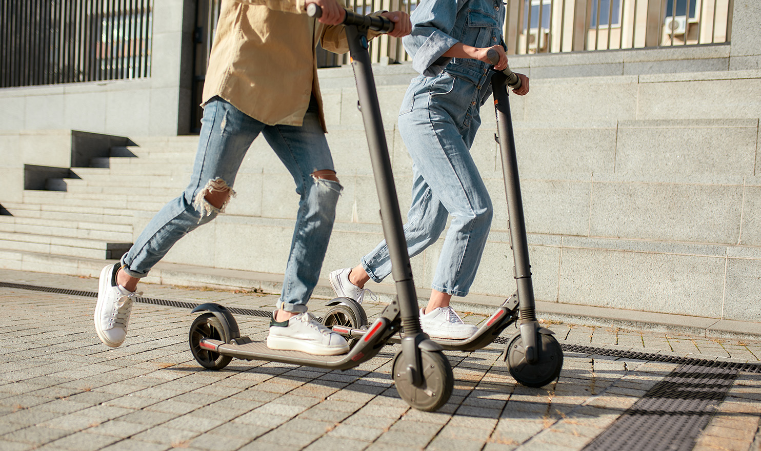 Two people riding on electric scooters on a public sidewalk.